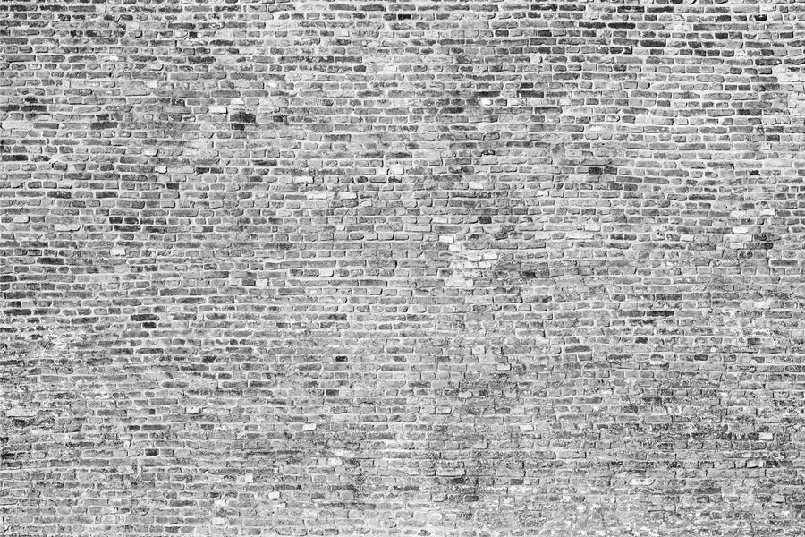 Modern open-plan living and dining area with wooden floors, blue armchairs, a Monochrome Brick Wall Wall Mural as an accent, sofa, rugs, long wooden dining table with chairs, pendant lights, kitchen in the background, and plants.