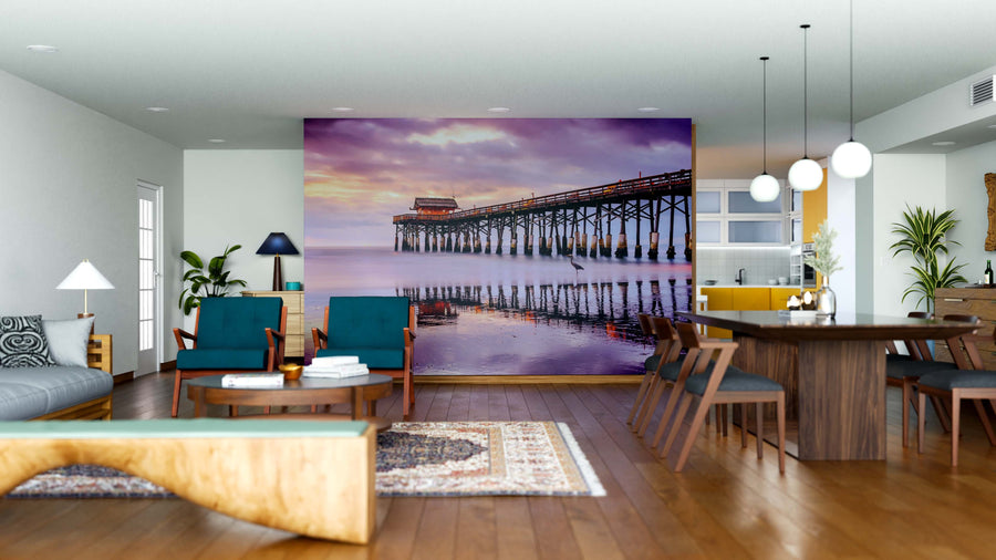 A modern open-concept living and dining room features the Cocoa Beach Wall Mural as a stunning focal point. Wooden floors, contemporary furniture, hanging lights, a cozy rug, and a sleek kitchen area complete the warm, inviting space.