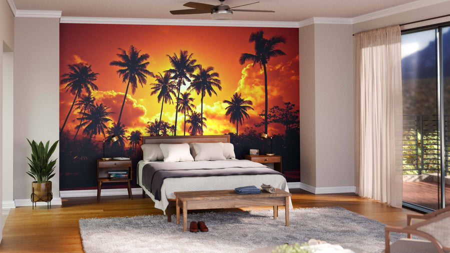 A modern open living-dining space features wood floors, teal chairs, a long dining table, pendant lights, and a Coconut Palms Wall Mural depicting palm trees at sunset, with a cozy kitchen in the background.