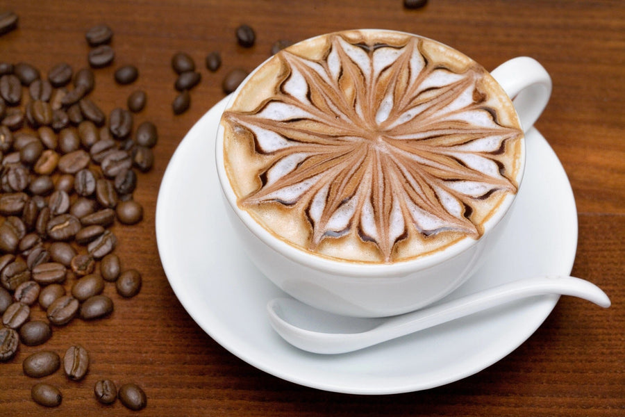 A modern café with wooden tables and stools, small potted plants on each table, pendant lights, and a large Coffee Beans Wall Mural featuring a cappuccino with latte art and coffee beans in the background.