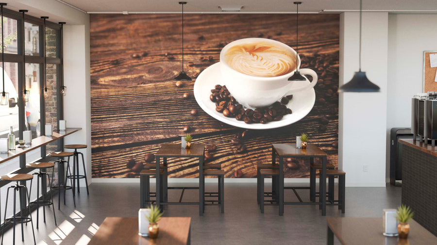 A modern café with wooden tables, barstools, potted plants on each table, and a Brown Coffee Wall Mural featuring a cappuccino with latte art on rustic wood surrounded by coffee beans. Natural light pours in through large windows.