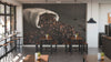 Modern coffee shop with wooden tables, black chairs, and potted succulents. The Burlap Bag of Beans Wall Mural shows roasted beans spilling from a sack. Industrial pendant lights hang above, and tall windows fill the space with natural light.