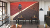 A modern café with wooden tables, stools, potted plants on each table, and a large Coffee Cherry Drying Wall Mural depicting a person in a blue hat sweeping red and brown material outdoors in straight lines.