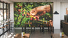 A modern café with high tables and stools features the Coffee Cherry Picking Wall Mural, showing hands picking ripe and unripe cherries. Large windows line the left side, and each table holds a small potted plant.