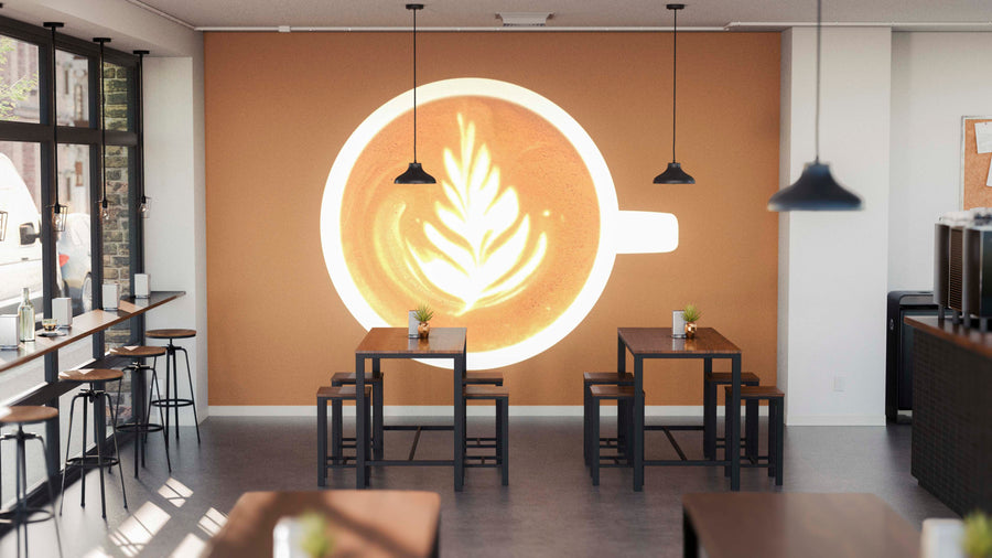 A modern café interior with wooden tables, stools, pendant lights, and large windows features the Art in Coffee Wall Mural—a giant print of a coffee cup with latte art. Small plants on each table add a fresh touch.