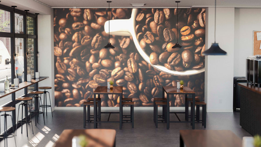 A modern coffee shop with wooden tables and chairs, pendant lights, and the Bean and Brew Wall Mural showing coffee beans with a metal scoop. Small potted plants accent the tables, while large windows fill the space with natural light.