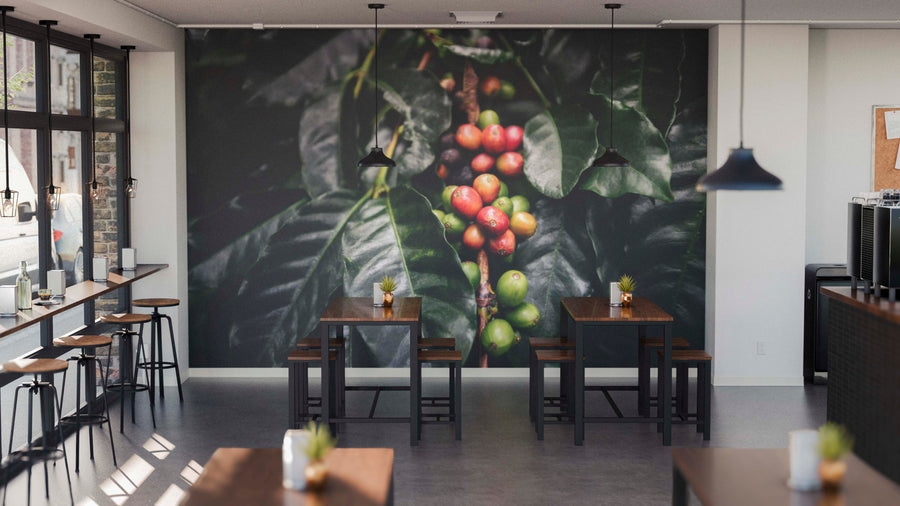 A modern café features wooden tables, stools, potted plants, and a Brew Roots Wall Mural with coffee cherries and green leaves. Pendant lights hang from the ceiling, while large left-side windows bring in natural light.
