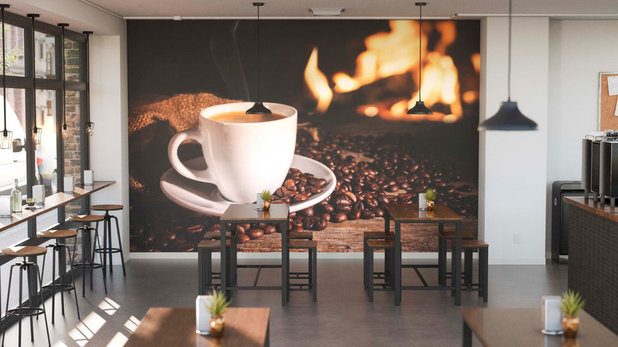 A modern café with wooden tables, stools, potted plants, and large windows. The back wall features the Cozy Coffee Wall Mural—a steaming coffee cup on beans by a warm fire—adding a cozy vibe to the space.