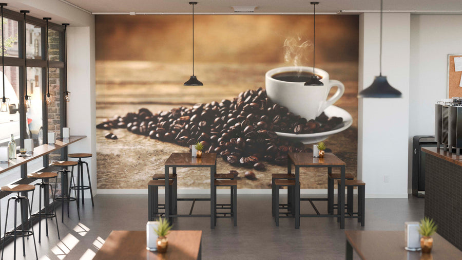 A modern café with wooden tables, stools, potted plants on each table, and large windows on the left. The back wall features the Cup of Coffee Wall Mural showing steaming coffee in a white cup beside beans on a rustic surface.