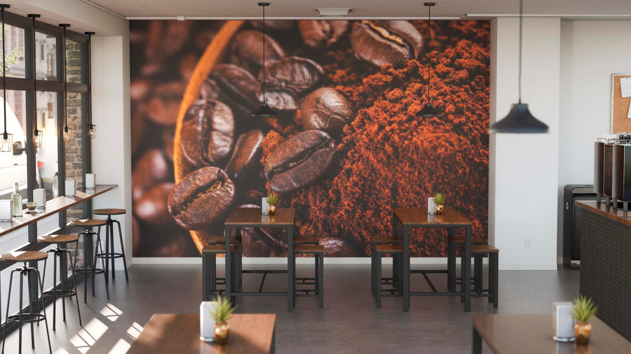 A modern café features wooden tables and chairs, potted plants, and large windows on the left. The back wall showcases the Dark Roast Perfection Wall Mural—depicting coffee beans and ground coffee—for a cozy, coffee-inspired vibe.