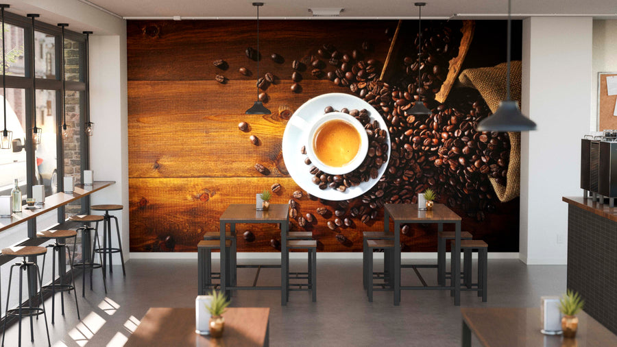 A modern café interior features tables, stools, large windows on the left, small plants, and a cozy custom-printed Espresso and Coffee Beans Wall Mural that adds warmth and charm to the inviting space.