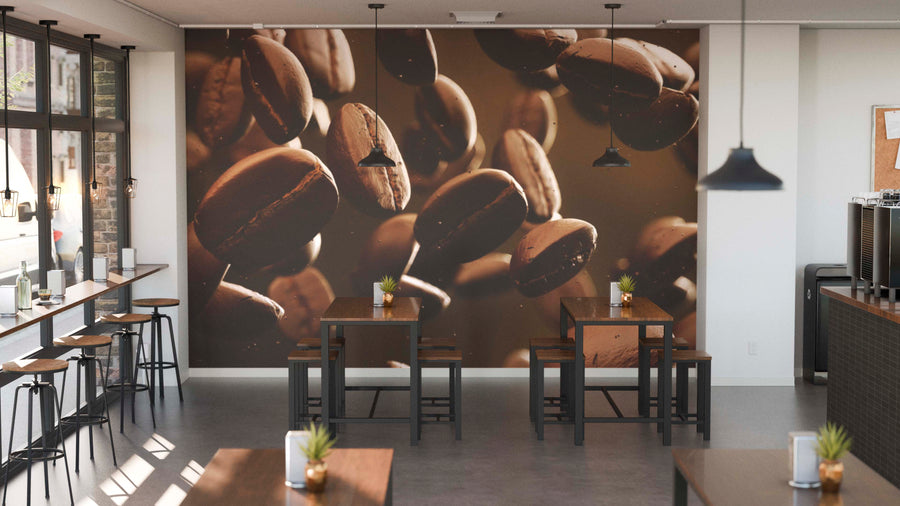 A modern café with wooden tables and black chairs features the Floating Coffee Beans Wall Mural as a focal point. Small potted plants decorate tables, pendant lights hang above, and daylight streams through large windows on the left.
