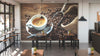 Modern café interior with wooden tables, small green plants, and a Fresh Brew Wall Mural featuring a frothy coffee cup, spoon, beans, and burlap sack. Pendant lights hang above as large windows fill the space with natural light.