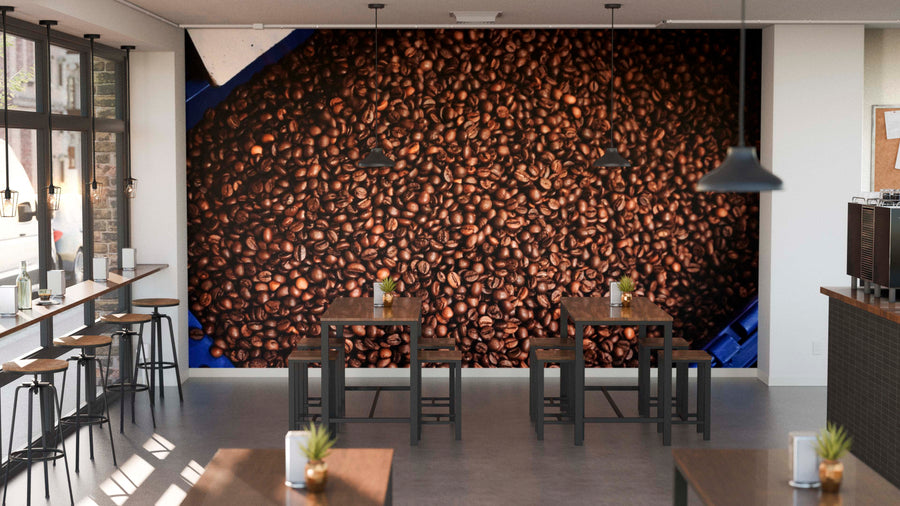 A modern café with wooden tables, stools, potted plants on each table, large windows on the left, and the Fresh Roasted Beans Wall Mural—a peel and stick mural of roasted coffee beans—covering the entire back wall.