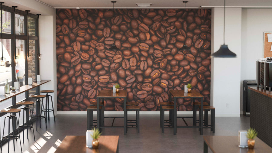 A modern coffee shop interior features wooden tables, potted plants, and a Fresh Whole Beans Wall Mural on the back wall. Pendant lights hang from the ceiling while sunlight pours in through tall windows on the left.