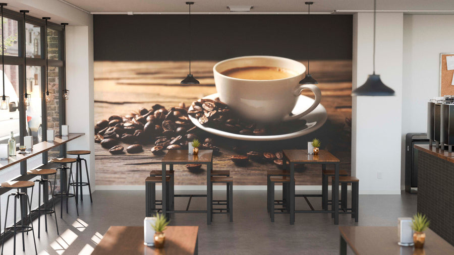 A modern café interior featuring wooden tables, stools, potted plants, hanging lights, and a Freshly Brewed Coffee Wall Mural displaying a close-up of a coffee cup on a saucer with beans scattered on rustic wood.