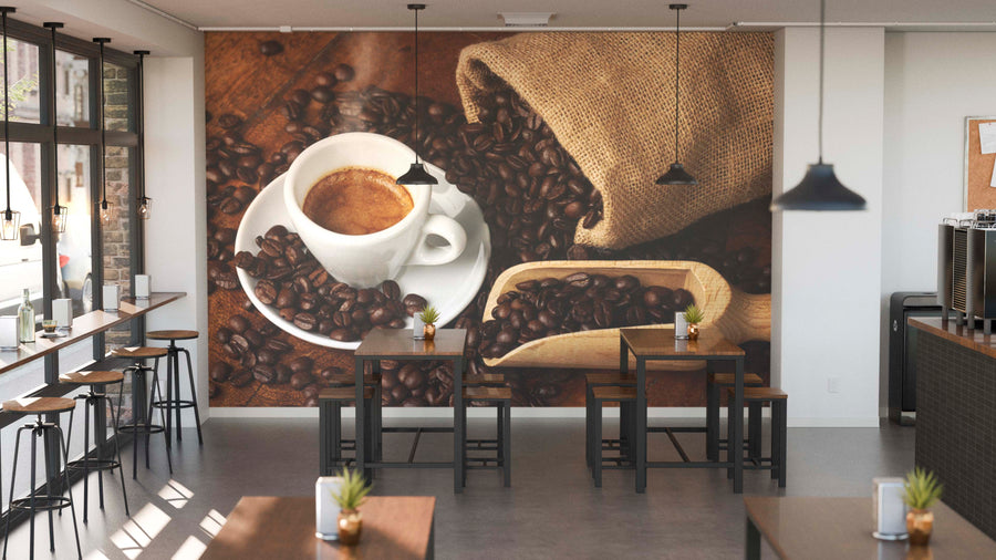 A modern coffee shop interior featuring wooden tables, stools, potted plants, large left-side windows, and the Freshly Brewed Espresso Wall Mural depicting a coffee cup with espresso, a wooden scoop, and spilled coffee beans.
