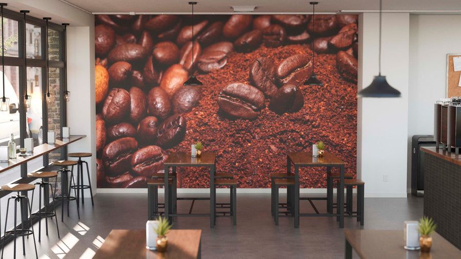 A modern café interior boasts the Freshly Roasted Coffee Beans Wall Mural. Wooden tables, stools, potted plants, pendant lights, and large windows on the left fill the space with natural light.