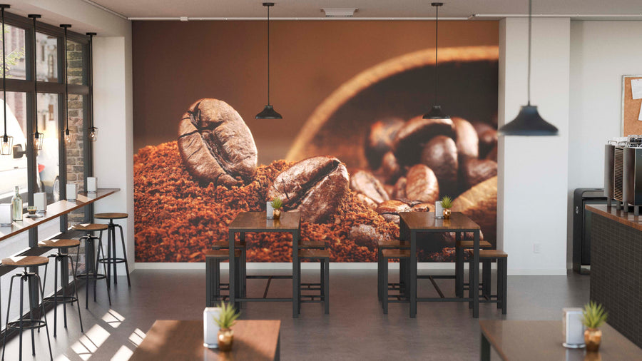 Modern café interior with wooden tables, black stools, pendant lights, and small potted plants. The Ground Coffee and Beans Wall Mural displays close-up coffee beans and ground coffee. Large windows on the left fill the space with natural light.