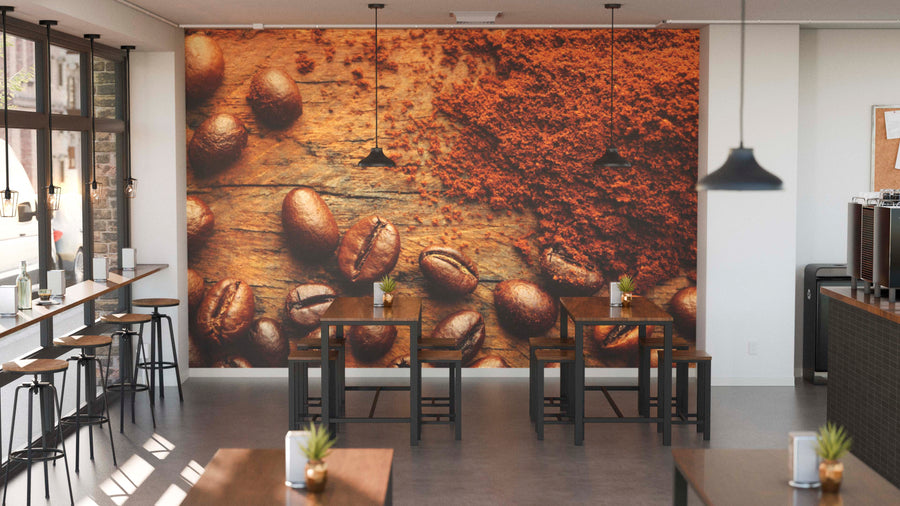 A modern café interior with wooden tables, black stools, pendant lights, and a striking Ground and Whole Beans Wall Mural on the back wall. Sunlight fills the space through tall windows, while small potted plants sit on each table.