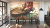 A modern café features the Hands at Work Wall Mural, showing a person sorting coffee beans in a woven basket. Wooden tables, stools, potted plants, and pendant lights complete the look as sunlight floods through tall windows.
