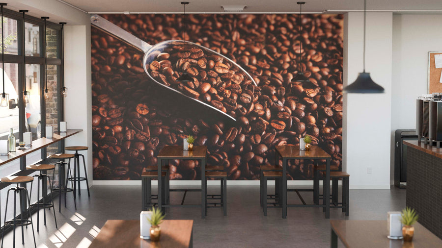 Modern coffee shop with wooden tables, stools, potted plants, and large windows. The back wall showcases the Harvested Coffee Display Wall Mural—featuring a metal scoop of roasted beans. Pendant lights add a cozy vibe to the space.