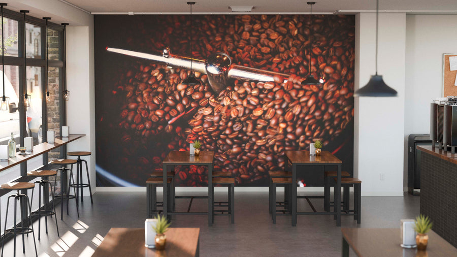 A modern café with high tables and stools features the Perfect Roast Wall Mural—a custom design of an espresso machine handle over coffee beans—on the back wall. Sunlight pours through tall windows, and small potted plants adorn the tables.