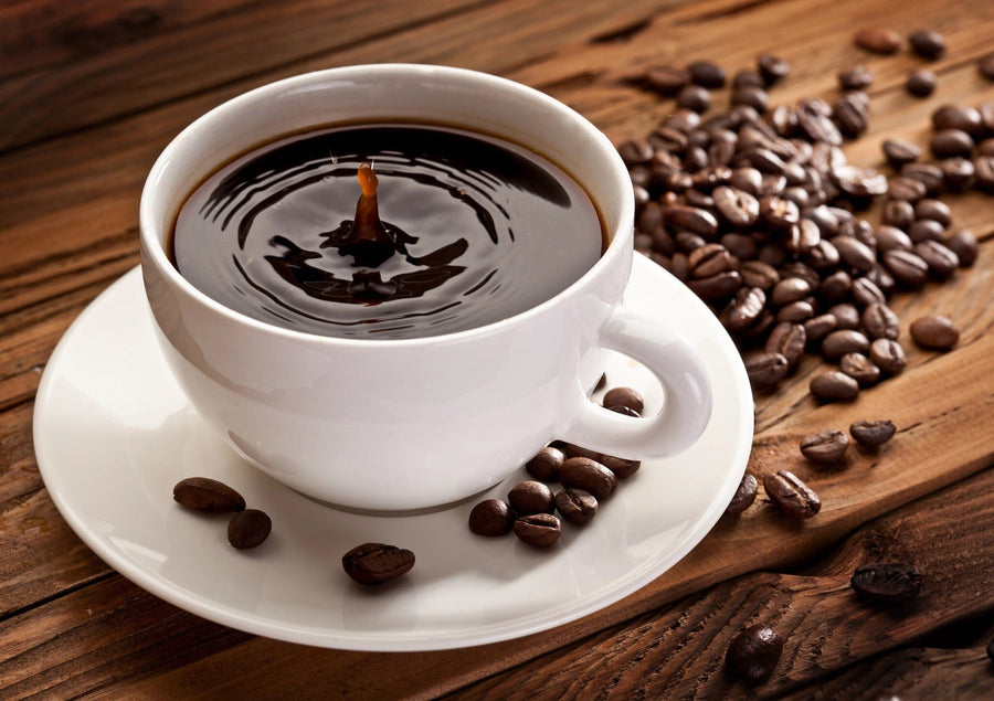 A modern café with wooden tables, stools, potted plant centerpieces, and large left-side windows. The back wall displays the Coffee Plant Wall Mural featuring a white coffee cup filled with coffee surrounded by coffee beans.