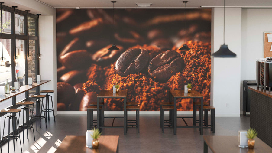 A modern coffee shop interior with wooden tables, black stools, small potted plants, pendant lights, and the Rich Coffee Grounds Wall Mural depicting close-up coffee beans. Sunlight streams in from large windows on the left.
