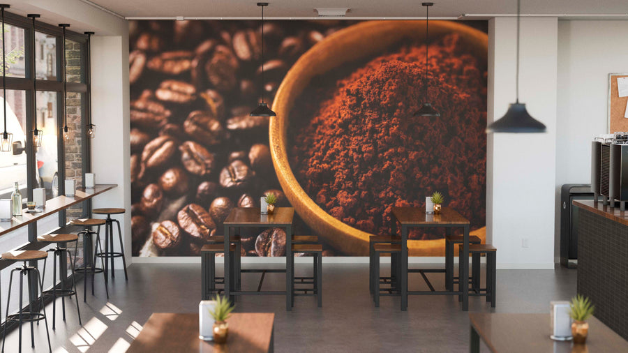 Modern café interior with tall windows, wooden tables and stools, and potted plants on each table. The back wall is decorated with the Rich Coffee Texture Wall Mural, featuring coffee beans and a bowl of ground coffee. Pendant lights create a cozy vibe.