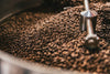 The Coffee Roast Wall Mural features a close-up of freshly roasted coffee beans in a metal roasting machine, with shiny rods and rich brown tones—ideal for custom printed murals or removable wallpaper, evoking the aroma and warmth of fresh coffee.