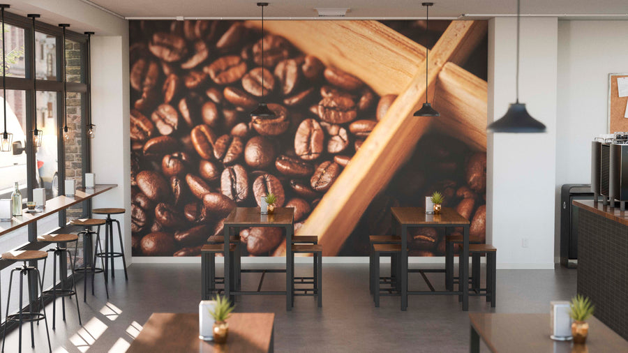 A bright, minimalist coffee shop features wooden tables and stools, potted plants, large windows, and the Roast in Motion Wall Mural—a custom print showcasing a close-up of coffee beans with a wooden scoop.