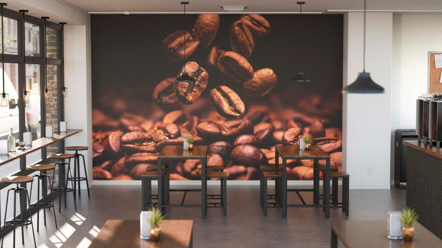 Modern coffee shop interior with wooden tables, black chairs, and potted plants. The back wall features a Roasted Coffee Bliss Wall Mural. Pendant lights hang overhead, and large windows on the left fill the space with natural light.