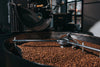 Close-up of the Coffee Roasting Process Wall Mural featuring a coffee roasting machine with rich brown roasted beans inside. Shiny metal arms stir the beans, while sunlight through a window illuminates the scene—ideal for custom printed murals.