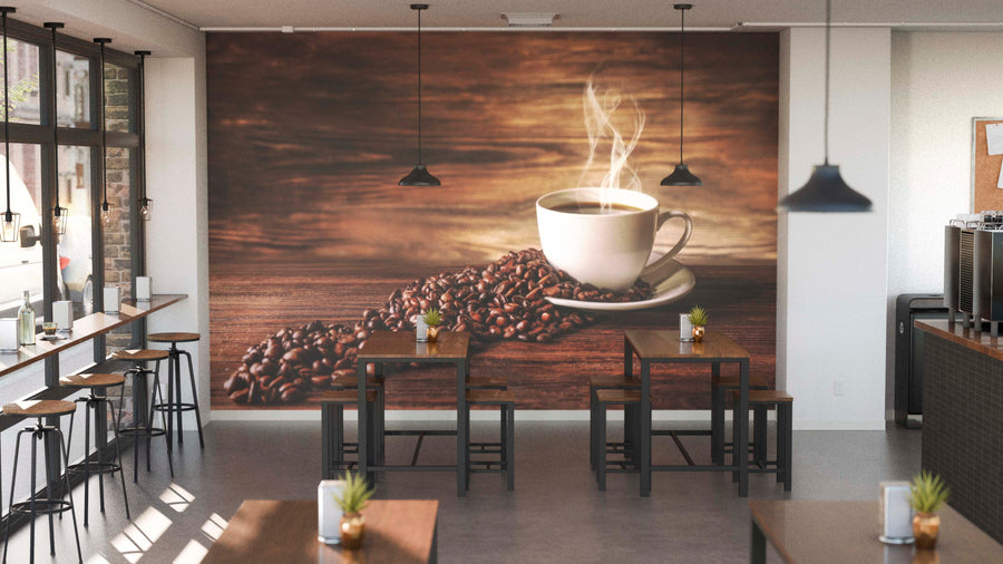 A modern coffee shop interior with wooden tables, black chairs, and hanging lights. The back wall features the Rustic Coffee Aroma Wall Mural of a steaming cup, while sunlight streams in and potted plants sit on each table.
