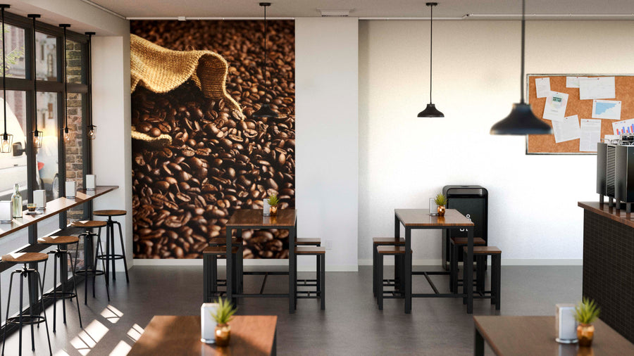 A modern coffee shop with wooden tables, bar stools by large windows, and a Spilled Coffee Beans Wall Mural. Hanging pendant lights, potted plants, and a bulletin board with papers enhance the bright, tidy atmosphere.