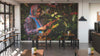 A modern café with wooden tables, stools, and potted plants features the Woman Picking Coffee Wall Mural—a peel and stick mural of a woman in a headscarf and plaid shirt examining coffee cherries amid lush greenery.
