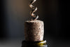 A close-up of the cork partially removed from a wine bottle by a metal corkscrew resembles an intricate scene from the Wine 18 Wall Mural. The natural cork contrasts with the dark green bottle lip, and a dark background enhances this dynamic focus moment.