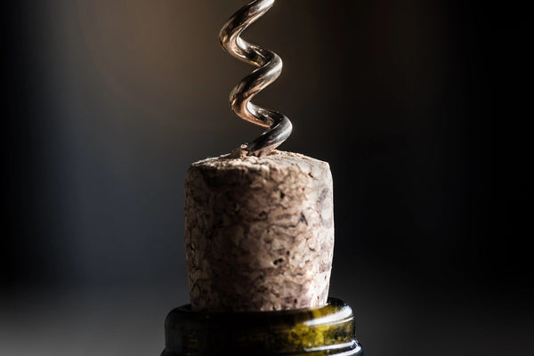 A close-up of the cork partially removed from a wine bottle by a metal corkscrew resembles an intricate scene from the Wine 18 Wall Mural. The natural cork contrasts with the dark green bottle lip, and a dark background enhances this dynamic focus moment.