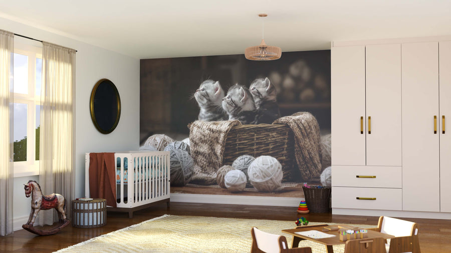 A cozy nursery with a crib, rocking horse, toys, and dresser features the Cozy Basket Kittens Wall Mural—a playful display of three kittens in a basket with yarn—which complements the room’s soft colors as daylight streams through the window.