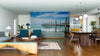 A modern open-plan living and dining room features mid-century furniture, wood accents, and the Crashing Waves Wall Mural, a peel and stick design that brings breezy coastal vibes and is easy to update with removable wallpaper.