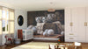 A cozy nursery with a crib, rocking horse, and toys features the Curious Tabby Trio Wall Mural showing three gray tabby kittens in a basket with yarn. Sunlight streams onto light wood floors, a soft rug, and white furniture with gold handles.