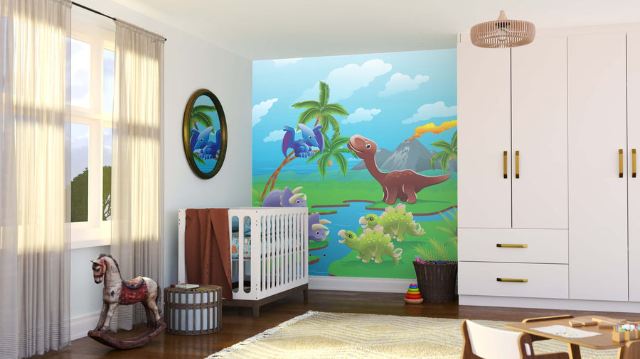 A nursery with a crib, round mirror, and the Dinosaur Island Fun Wall Mural featuring cartoon dinos, trees, and a volcano. Sunlight streams through sheer curtains onto toys on the wooden floor by white cabinets with gold handles.