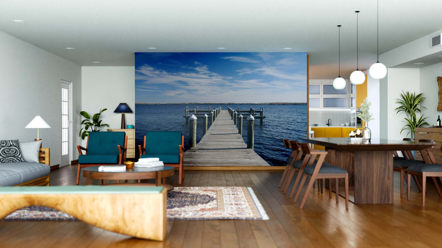 Modern open-concept living and dining space with wooden floors, blue and wood furniture, and the Dock Wall Mural—a large mural of a dock over calm water under a bright sky—creating a serene focal point in the room.