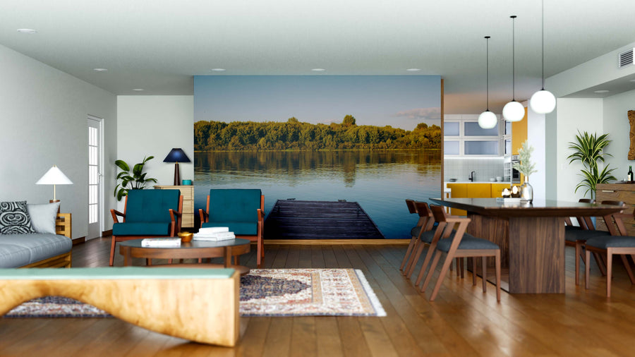 Modern open-plan living and dining room with wooden floors, teal chairs, pendant lights, and a Dockside Reflections Wall Mural depicting a serene lake with dock and trees. The kitchen in the background features yellow accents.