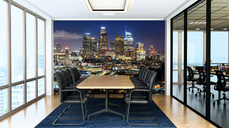 A modern conference room features a long wooden table, black chairs, floor-to-ceiling windows, and a Downtown LA Wall Mural on the far wall showcasing a city skyline at night with illuminated skyscrapers and bright lights.