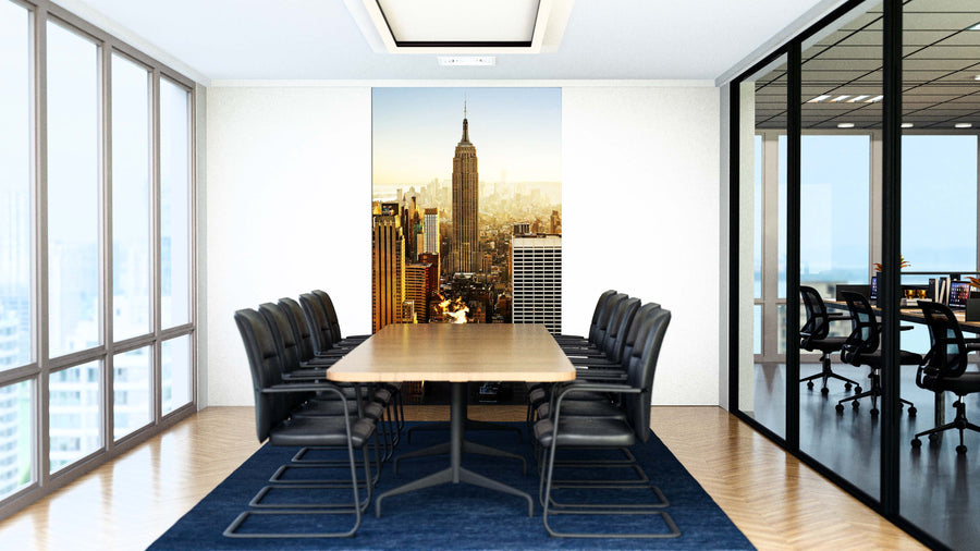 A modern conference room features a long wooden table, black chairs, and large windows. A wall displays the Empire Wall Mural of the Empire State Building and NYC skyline. Another meeting room is visible through glass walls.