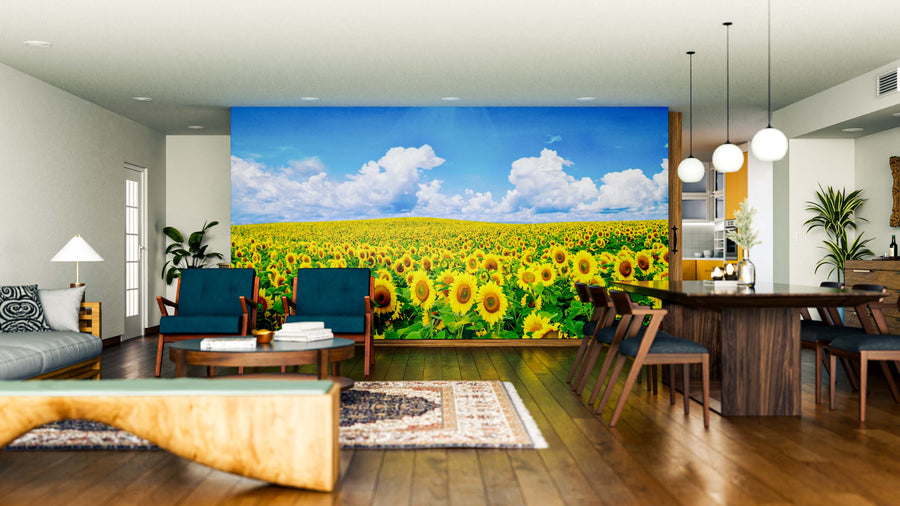 A modern living-dining room with wood furniture and green chairs features the Endless Sunflower Wall Mural on the back wall, adding a vibrant, nature-inspired focal point of sunflower fields beneath a blue sky to the bright, airy space.