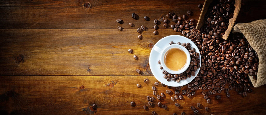 A modern café interior features tables, stools, large windows on the left, small plants, and a cozy custom-printed Espresso and Coffee Beans Wall Mural that adds warmth and charm to the inviting space.