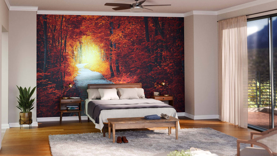 A cozy bedroom with a bed, wooden furniture, potted plants, and large sheer-curtained windows. Behind the bed, the Fantastic Autumn Forest Wall Mural displays a sunlit path through autumn trees above a soft area rug.